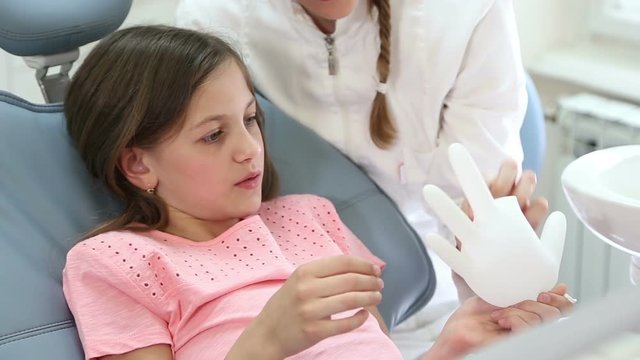 Close up of pretty girl and beautiful female dentist playing with rubber glove