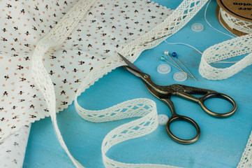 White lace ribbons on blue wooden background with with scissors and cotton fabric