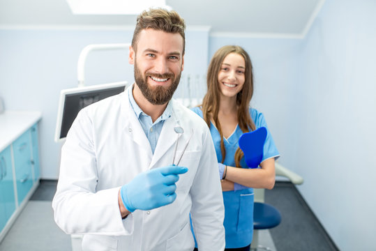 Portrait of handsome dentist with young female assistant in uniform at the dental office