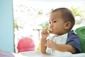 Asian baby eating food by himself