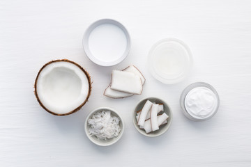 Homemade coconut products on white wooden table background. Oil, scrub, milk and lotion from top view. Good for space and background.
