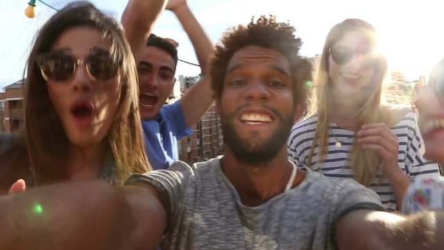 Close up of crazy multi-ethnic group of friends filming themselves at rooftop party on sunny day