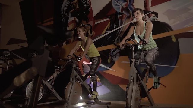 Young women riding stationary bicycles in fitness center