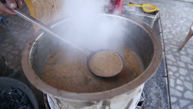 Man pouring chai with spoon from pot on heater at stand in Jodhpur.