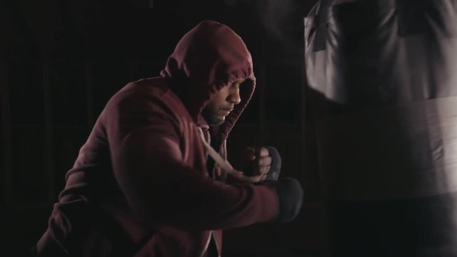 Boxer training on a heavy bag in a dark gym.
