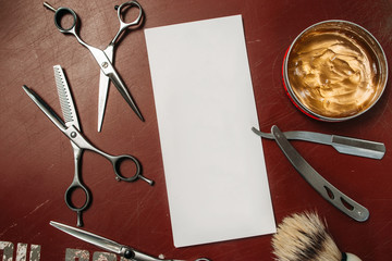 Blank card with barber tools flat lay. Top view on red table with scissors, razor, hair wax and shaving brush with empty white paper, free space. Barbershop, manhood concept