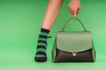 Two-colored photo: green and black handbag and woman's hand holding it on a green background. 