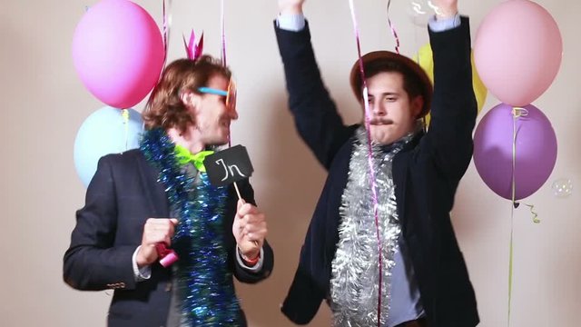 Two funny men holding boards in love in party photo booth 