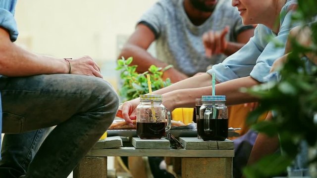 Mid-section view of young people sitting around table eating pizza and drinking cocktails, graded