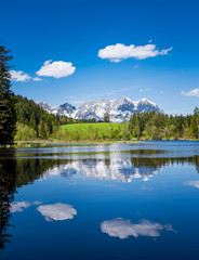 Snowy mountain range and clouds are reflected in a small lake near Kitzbuehel, Tyrol, Austria
