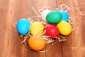 painted easter colorful eggs with straw nest on wooden background