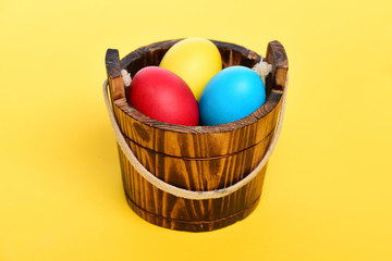 painted easter colorful eggs in wooden bucket on yellow background