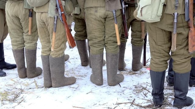 Soldiers in uniform during the second world war stand in the snow. Boots, shovels, jackets, and weapons.