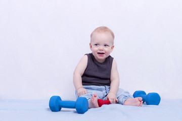 Smiling adorable 10 month boy sitting with dumbbells and looking at camera man