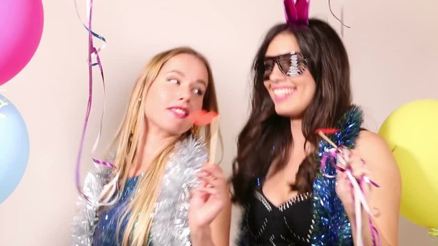 Two beautiful female friends having fun dancing with props in party photo booth 