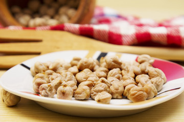 Wooden bowl with chickpeas and spoon on wooden table with red tablecloth