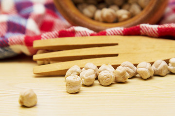 Wooden bowl with chickpeas and spoon on wooden table with red tablecloth