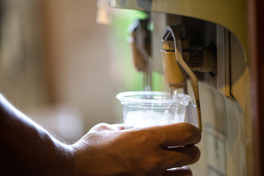 Male hand serving water of a water cooler in plastic cup.