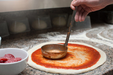 Male chef smears red sauce spicy pizza. Raw dough preform. Production and delivery of pizza
