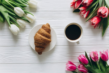 Cup of coffee with croissant and fresh tulips on wooden background for Mother's Day.