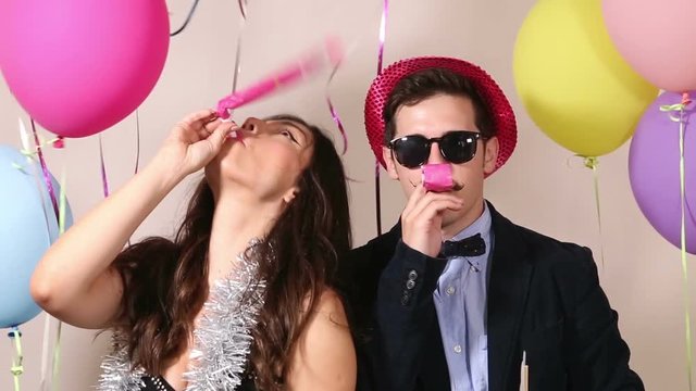 Cute couple having fun blowing party horn in photo booth