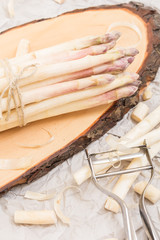 Bunch of white asparagus on  wood slice cutting board with metallic peeler,  on crumpled paper