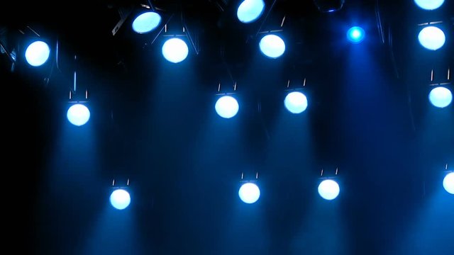 The blue light from the spotlights through the smoke on stage during a performance or show. Lighting equipment. The footage is looped without gaps.