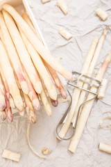 Bunch of white asparagus in box, on crumpled paper with metallic peeler.