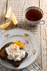 eggs pashot on a toast and tea with lemon on a wooden table