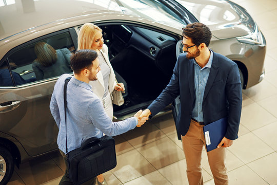 Young couple shaking hands with sales agent after a successful car buying