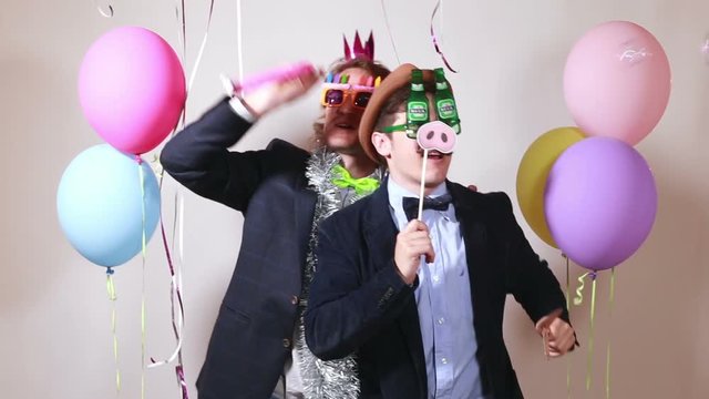 Two funny male friends having fun with props in photo booth