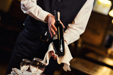 The waiter offers visitors wine,Waiter in uniform waiting an order,Waiter with a white towel on his hand,Confident waiter,A pub.Restaurant.Classic.Evening.European restaurant © bondvit