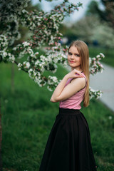 Fototapeta na wymiar Charming girl in pink blouse and black skirt poses for photographers on the background of beautiful flowering trees. Spring. Sakura.