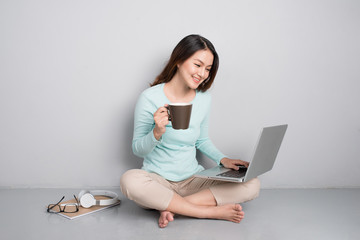 Obraz premium Happy casual beautiful asian woman working on a laptop sitting on floor at home.