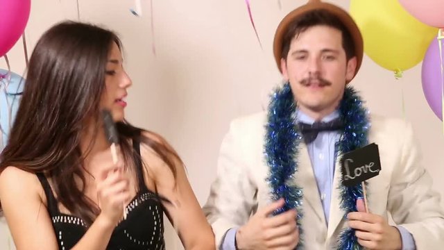 Funny party couple having fun dancing and holding in love boards in photo booth