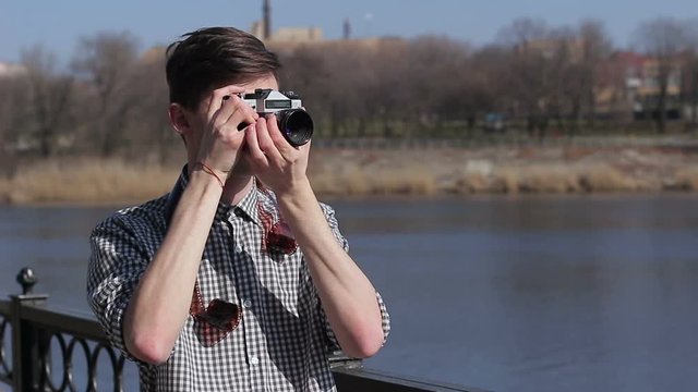 The young guy takes pictures on the old film camera on the river
