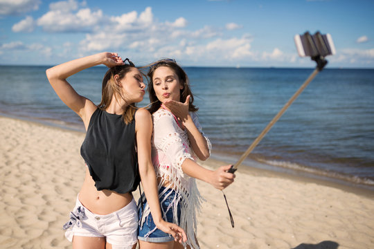 Two female friends taking selfie on beach sending kisses