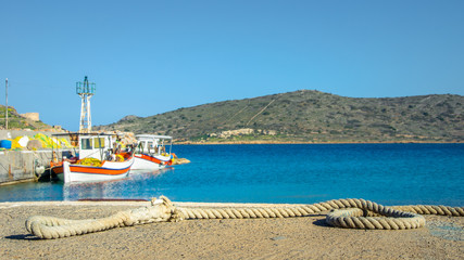 The small harbor of Plaka with traditional fishing boats, sailing rope on the dock, and the island of Spinalonga at the background, Crete, Greece.