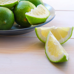 Fresh organic limes with slices in ceramic plate on wooden table. Limefruit background with copy space.