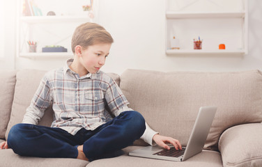 Child boy using laptop on couch at home