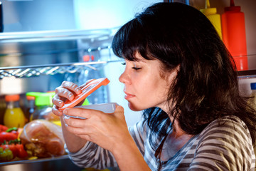 Woman opened the refrigerator and sniffs a container of food