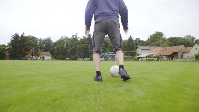 Following ordinary person kicking soccer ball on field 4K
