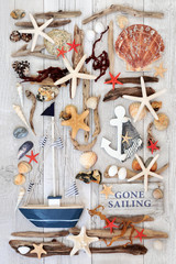 Sailing Themed Seaside Abstract. With decorative rustic wooden boat and sign with seashells, driftwood, seaweed and rocks.