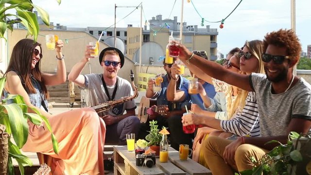 Group of happy multi-ethnic friends looking at camera and toasting with cocktails at rooftop party on beautiful sunny day