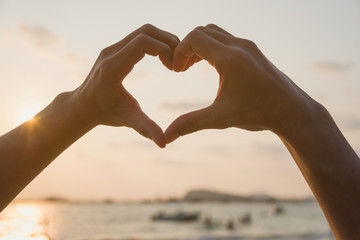 Beautiful woman hands making a heart shape with sea background on sunset