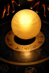 woman - fortune teller - with hands over crystal ball with fire yellow light over horoscope with astrology and zodiac signs 