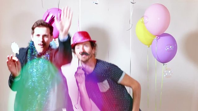 Two smiling happy men dancing with props in photo booth, graded