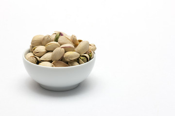 Pistachios in ceramic bowl on white background.