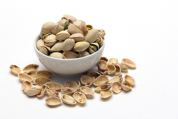 Ceramic bowl filled with pistachios on white background.
