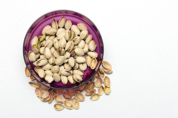 A shot from top, pistachios on white background in a purple bowl.